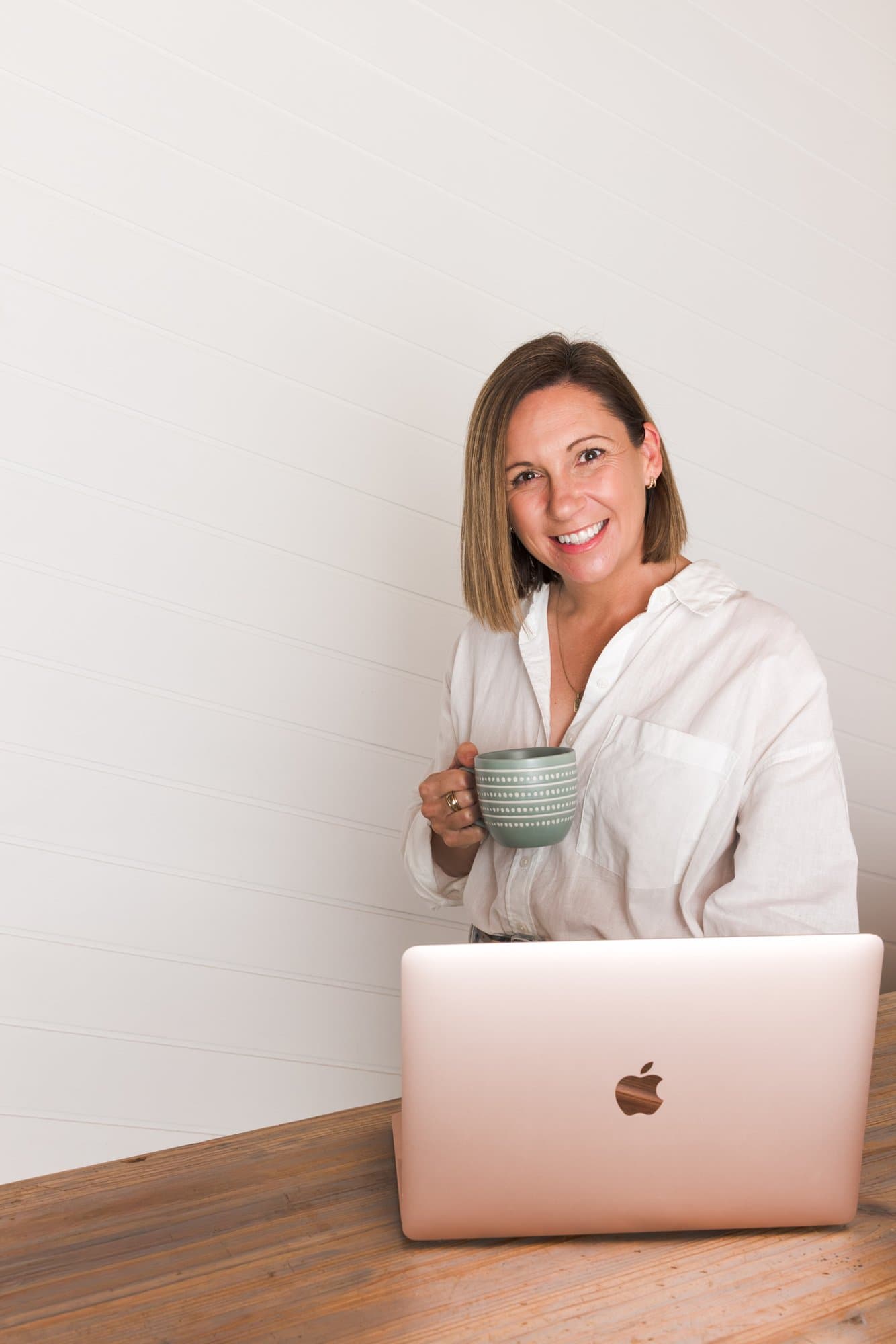 Steph smiling with a cup of tea, laptop on the table in front of her
