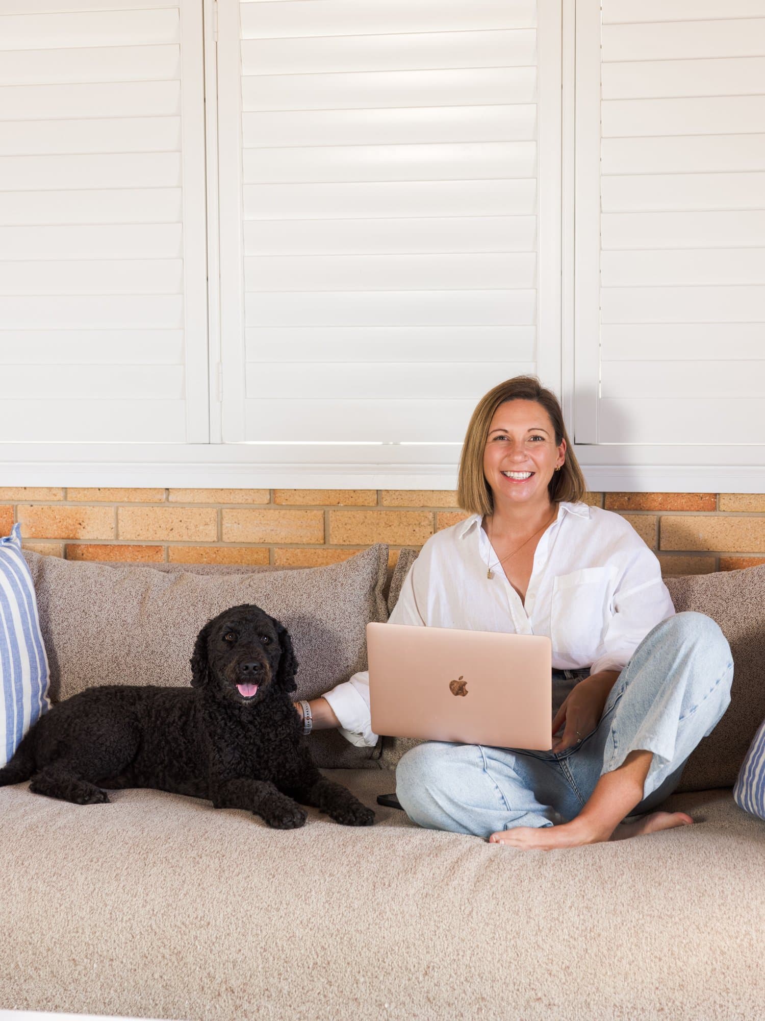 Steph on the couch with her laptop, her dog lying beside her