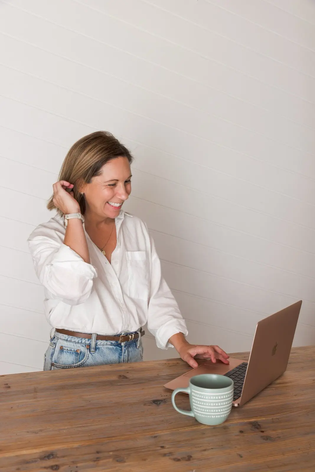 Steph laughing at her desk with a mug and her laptop